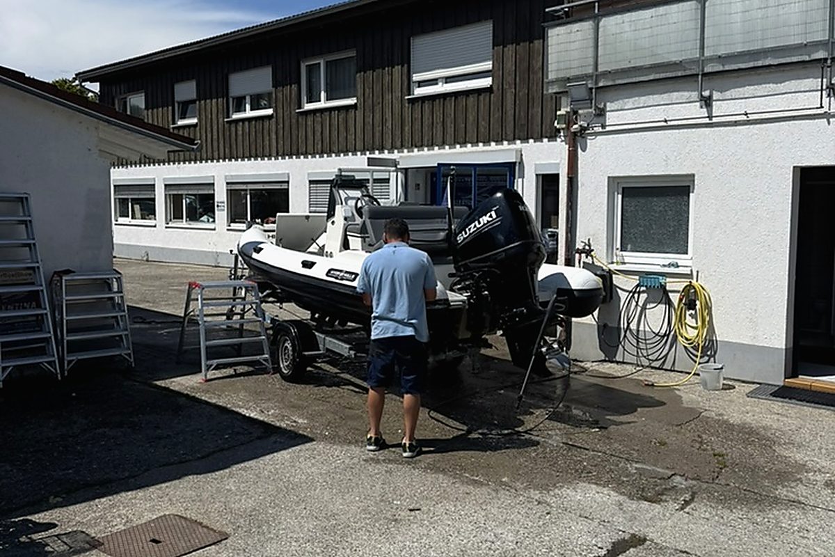 Mitarbeiter reinigt ein RIB mit Suzuki-Außenborder auf dem Trailer vor der Werkstatt
